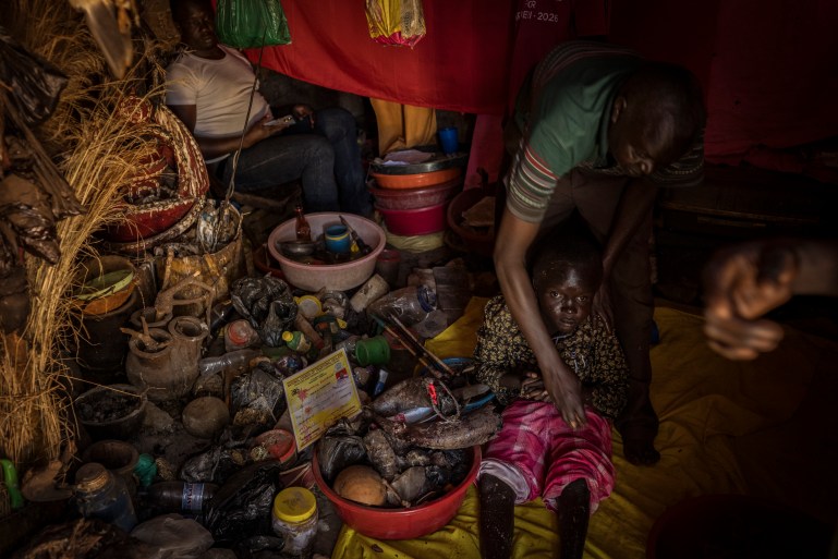 Omalera ، منطقة سوروتي ، أوغندا. الطبيب الساحر المحلي روبرت أبيدو يعالج نوح أويار ، 17. نوح لا يستخدم ساقيه ويعيش أيضًا مع استسقاء الرأس. عالج روبرت هذه الظروف عن طريق فرك معجون الماء والمواد النباتية في الجلد نوح. في حين أنه معروف جيدًا في المنطقة كطبيب ساحر ، إلا أنه يفهم الدلالة السلبية المحيطة بمهنته ، مثل العديد من الآخرين الذين يشيرون إلى نفسه على أنه 