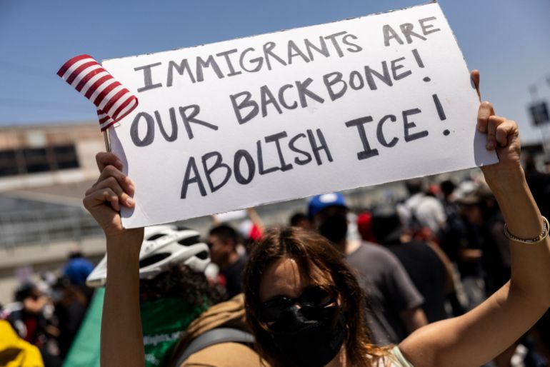 A demonstrator holds a poster reading “Immigrants are our backbone! Abolish Ice!” in front of National guards during clashes with law enforcement in front of the federal building during a protest following federal immigration operations, in Los Angeles, California on June 8, 2025.