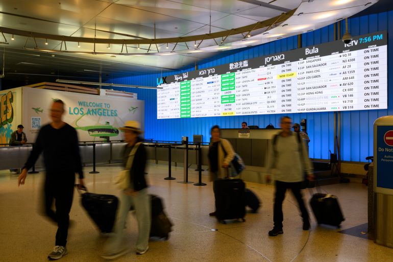 Travelers cart their luggage through the international arrivals area at the Los Angeles International Airport in Los Angeles, Saturday, June 8, 2025. (AP Photo/William Liang)