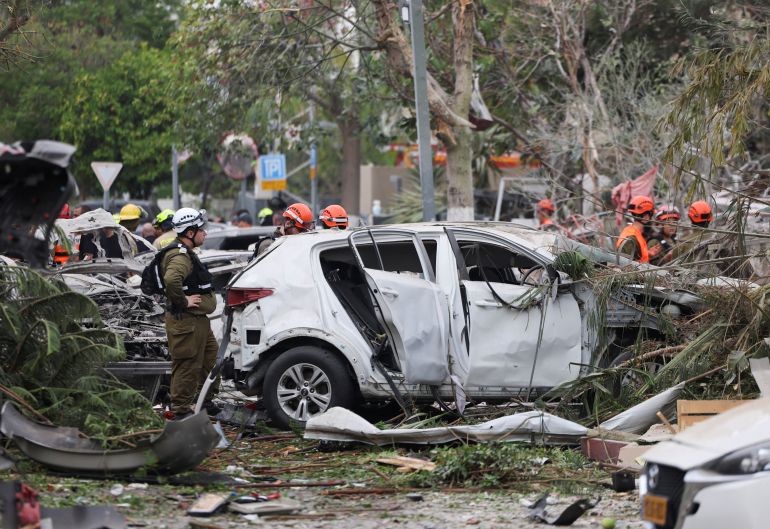 Rescue personnel stand next to damaged vehicles as they work at an impact site following missile attack from Iran on Israel, in Rishon LeZion, Israel, June 14, 2025. REUTERS/Ronen Zvulun