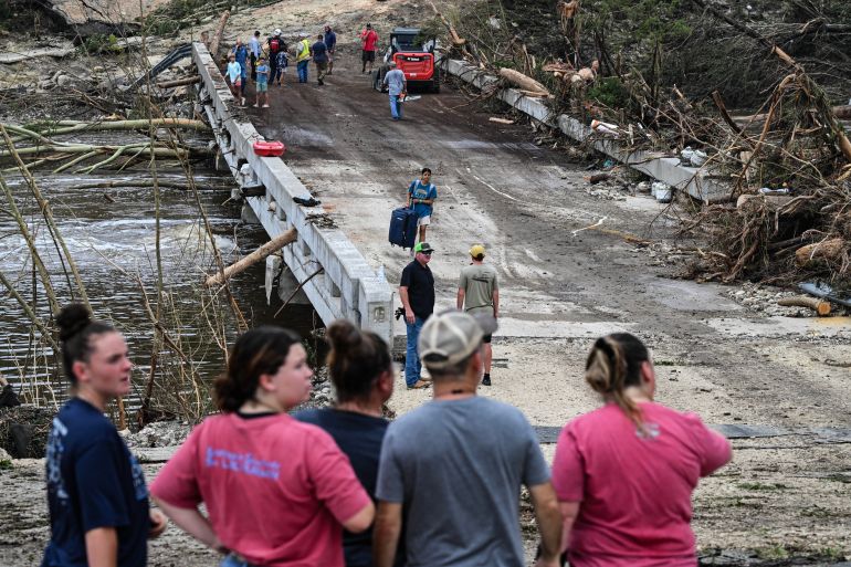 TOPSHOT - People look on as law enforcement and volunteers continue to search for missing people near Camp Mystic, the site of where at least 20 girls went missing after flash flooding in Hunt, Texas, on July 5, 2025.