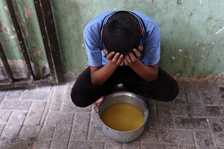 A displaced Palestinian child sits next to a pot of lentil soup that he received at a food distribution point in Gaza City in the northern Gaza Strip on July 25, 2025.