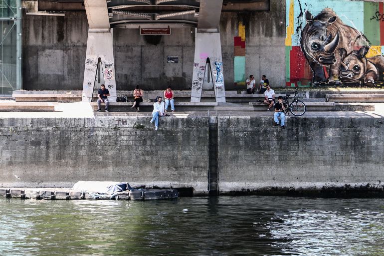 People sit in the shade under a bridge over the River Seine in Paris, on June 30, 2025, during a heat wave in France.