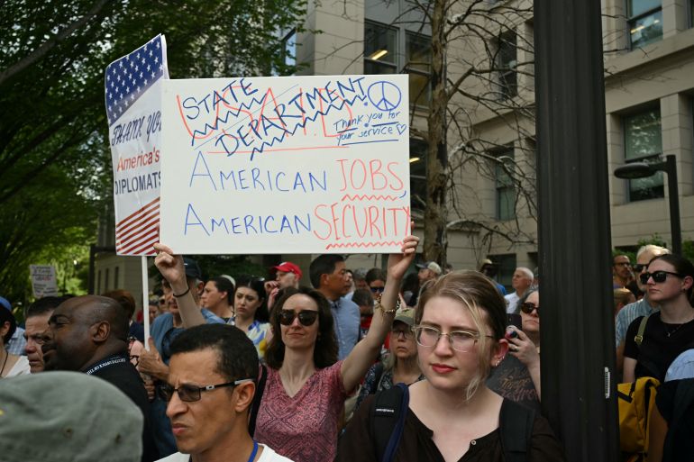 Supporters of fired US State Department workers hold signs outside the building in Washington, DC, on July 11, 2025. The US State Department began laying off more than 1,300 employees as part of President Donald Trump's campaign to massively downsize the federal government workforce. A State Department official said 1,107 members of the civil service and 246 Foreign Service employees were being informed that they were being fired. (Photo by SAUL LOEB / AFP)