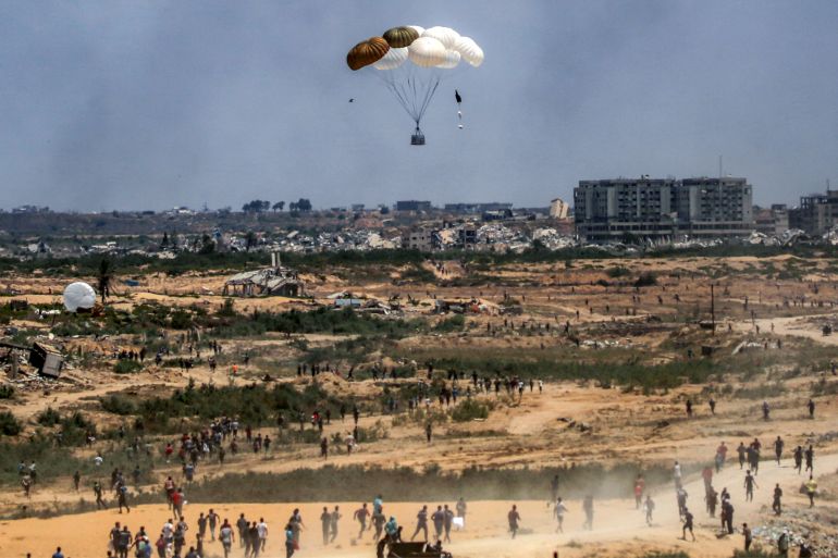 TOPSHOT - Palestinians rush to the scene as air pallets, carrying humanitarian aid, parachute down after being dropped from a military plane over Nuseirat in the central Gaza Strip during an airdrop mission above the Israel-besieged Palestinian territory on August 5, 2025.
