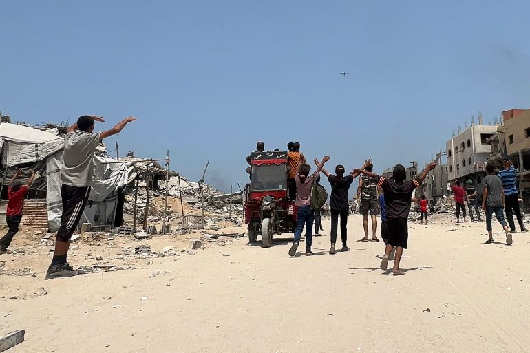 Palestinians wave as a military aircraft conducting an airdrop of humanitarian aid approaches, in Jabalia in the northern Gaza Strip on August 9, 2025.