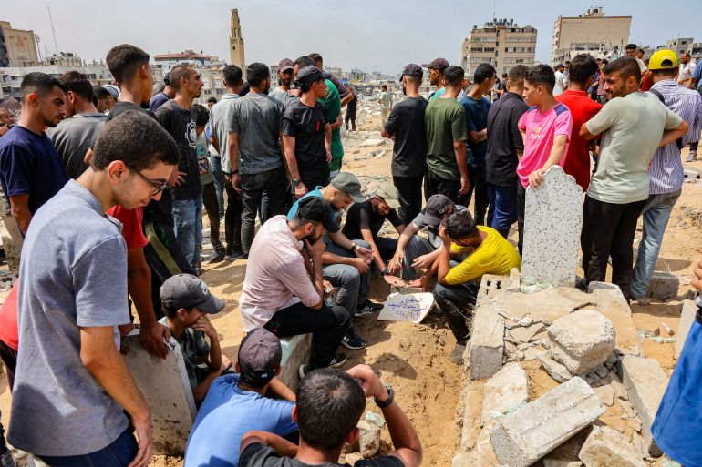 TOPSHOT - Mourners sit around the grave of Al Jazeera correspondent Anas al-Sharif, who was killed alongside other journalists in an overnight Israeli strike on their tent in Gaza City, following his burial at the Sheikh Radwan cemetery in Gaza City on August 11, 2025.
