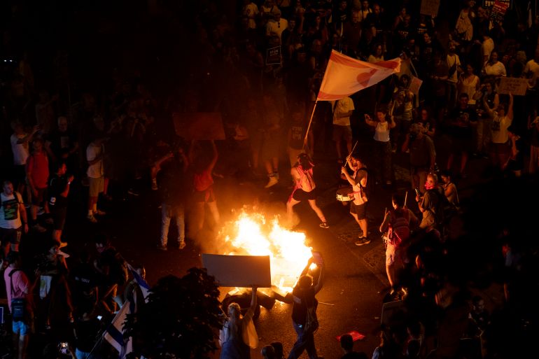 TEL AVIV, ISRAEL - AUGUST 7: Protesters set a fire as they hold signs and flags during a protest calling for a hostages deal on August 7, 2025 in Tel Aviv, Israel. Local media reports that Israeli Prime Minister Benjamin Netanyahu is seeking backing from his security cabinet for the "full occupation" of the Gaza Strip, despite warnings from security officials and human rights groups that such a move could further endanger the lives of hostages still believed to be held alive by Hamas, as well as Palestinians already suffering displacement and an acute hunger crisis in Gaza. (Photo by Amir Levy/Getty Images)