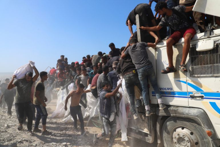 A Palestinian man carries aid that entered Gaza through Israel, as other Palestinians ride on a truck, in Beit Lahia in the northern Gaza Strip, August 3, 2025. REUTERS/Ebrahim Hajjaj