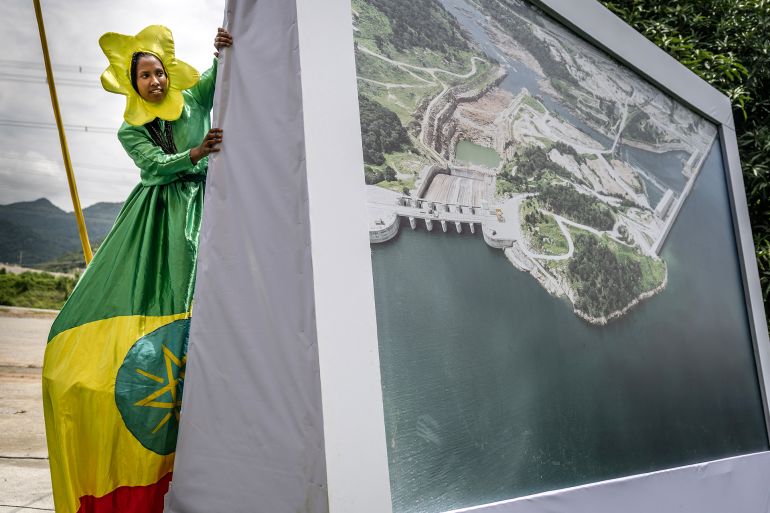 A member of an acrobat group prepares to perform, dressed in the Ethiopian flag colours, behind a decorative aerial image of the Grand Ethiopian Renaissance Dam (GERD) during its official inauguration ceremony in Guba, on September 9, 2025