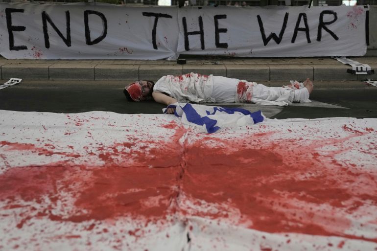 A demonstrator lies on the ground painted in red, symbolizing blood, during a protest demanding the end of the war, the immediate release of hostages held by Hamas in the Gaza Strip, and against Prime Minister Benjamin Netanyahu's government in Tel Aviv, Israel, Saturday, Aug. 16, 2025. (AP Photo/Mahmoud Illean)